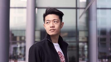 Asian guy wearing a black leather jacket, looking over his shoulders.