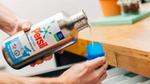  Image shows hands holding a Persil aluminium refill bottle pouring out detergent into a plastic lid]