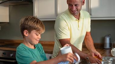 Father and young son in a kitchen doing the washing up together