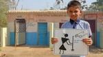 A schoolboy stands in front of a block of toilets holding a hand-drawn poster