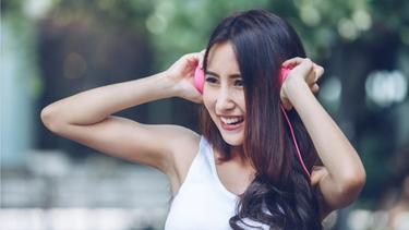 An Asian girl with long hair, wearing a white top, is listening music with a headset.