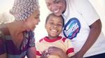 Two women, one wearing a Domestos t-shirt, laughing with a young child