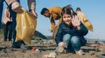 A young girl holding a rubbish bag, waving as she collects rubbish off a beach
