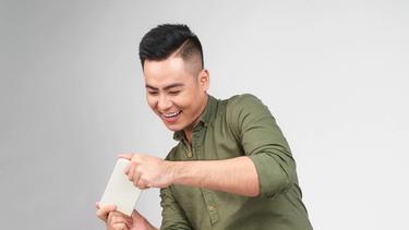An Asian guy wearing a green polo is playing with what appears like a white mobile phone. 
