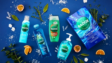 Five Radox products shown on a blue background with herbs, fruit, and salt scattered around