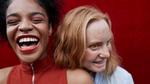 Close up shot of two women laughing against a red background
