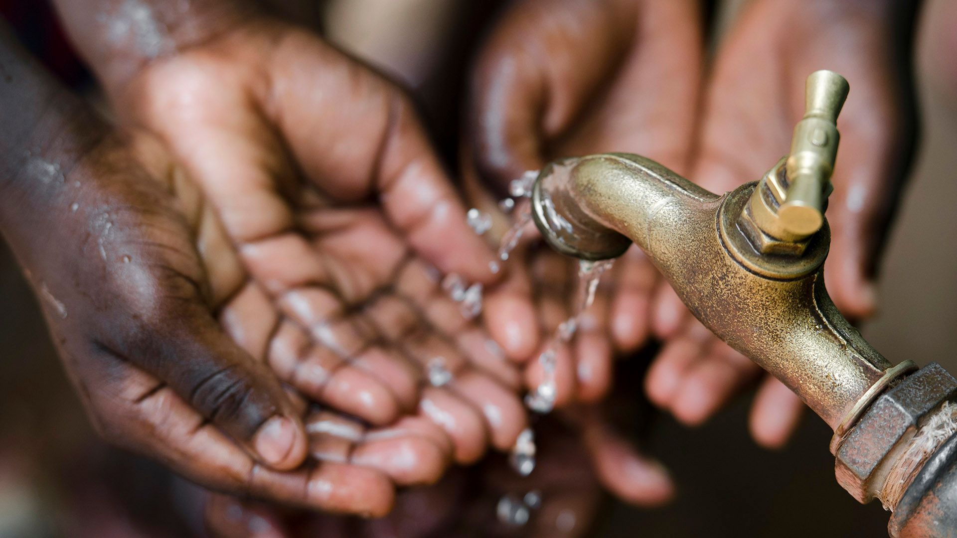 Two pairs of hands washing under a village tap