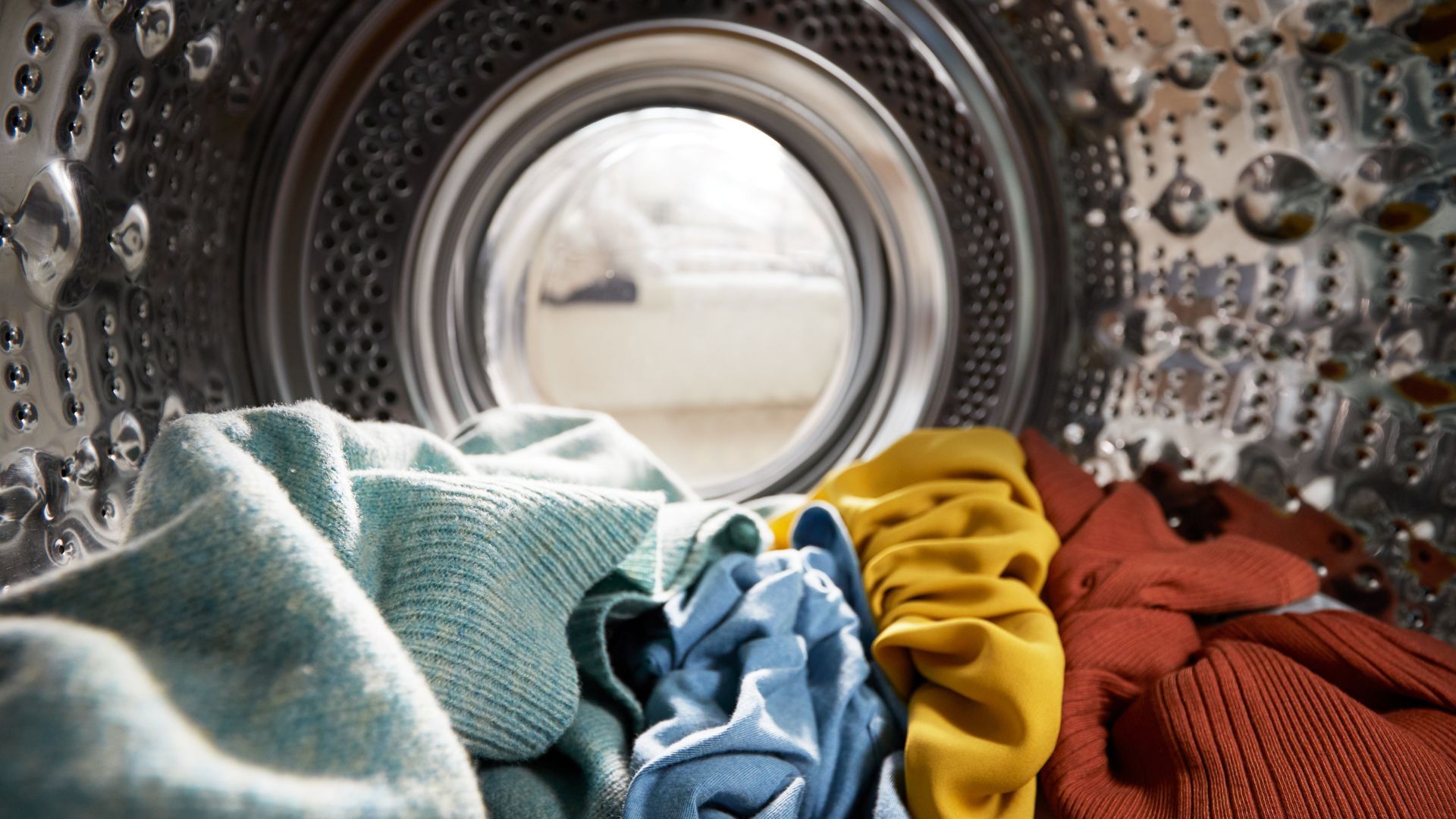 View of the inside of the drum of a washing machine showing a pile of brightly coloured clothes.
