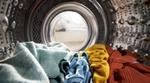 View of the inside of the drum of a washing machine showing a pile of brightly coloured clothes.