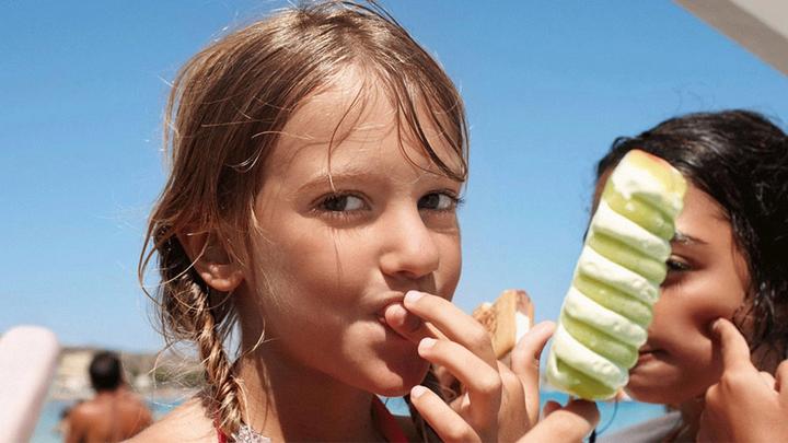 Gros plan d'une jeune fille sur une plage en train de manger une glace verte et blanche.