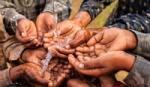 Children bring their hands together to hold some flowing water.