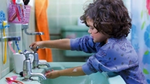 Young boy with curly hair runs water from a bathroom sink