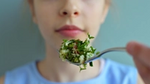 A young girl holding a spoon of salad in front of her