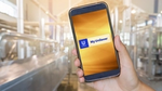 A hand holding an iPhone with a yellow screen with the Unilever logo and words ‘My Unilever’ against a blurred factory background.
