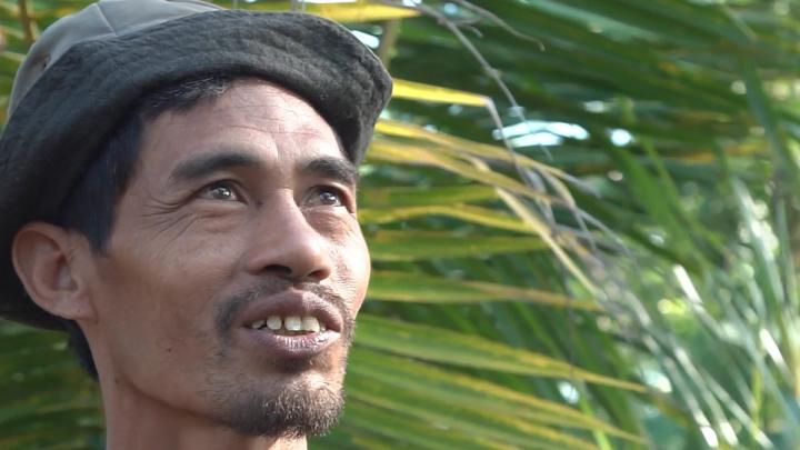 Coconut sugar farmer standing in front of a coconut tree.
