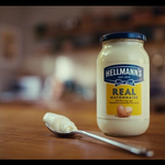 A jar of Hellmann’s mayonnaise with a spoon on a wooden table