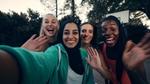 Four women of different races and religion smile and wave to the camera