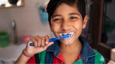 An Asian boy cleaning his teeth and smiling