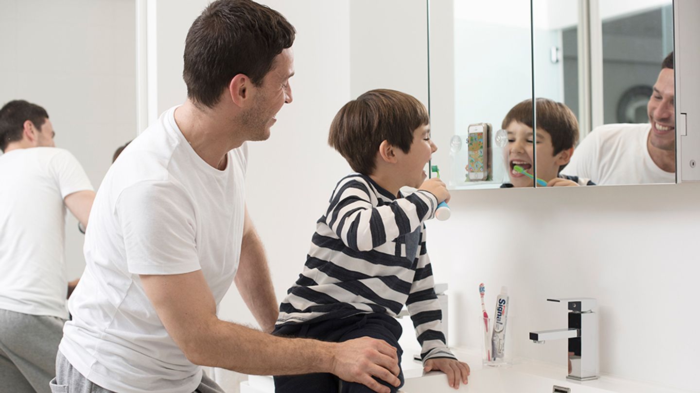 A father with child brushing his teeth and looking in mirror