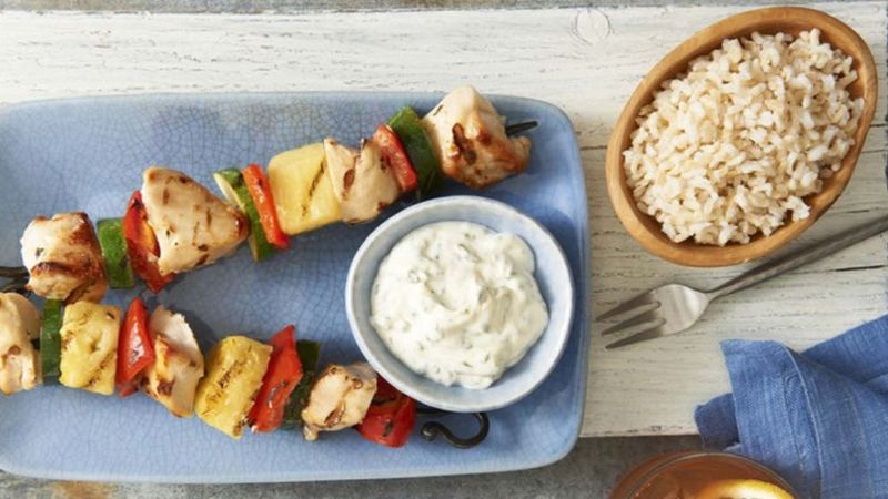 Picture of cilantro lime pinapple chicken skewers on a plate with rice in a bowl and fork