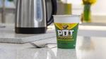 A Chicken & Mushroom Pot Noodle sitting on a grey kitchen counter, with a fork and kettle.