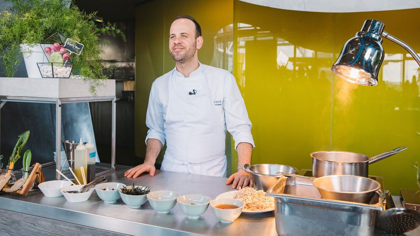 Michelin-starred chef Gregory Marchand stands behind a kitchen worktop bowls of a variety of ingredients