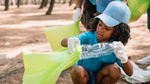 A child in a blue cap picking up plastic from a beach