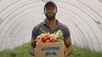 Man in baseball cap carrying vegetables in a cardboard box with Hellmann’s logo