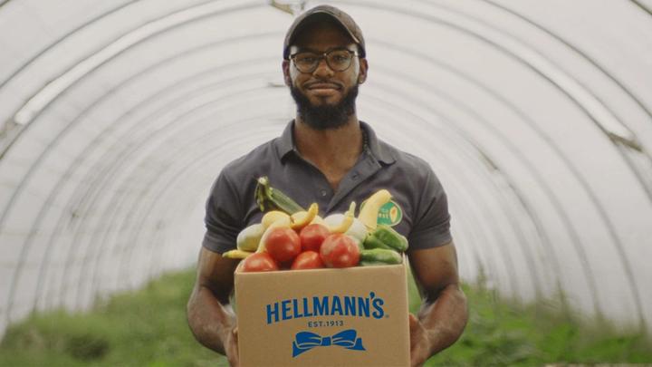 Man in baseball cap carrying vegetables in a cardboard box with Hellmann’s logo