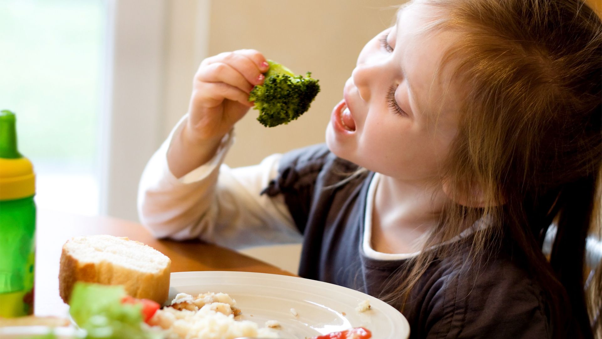 Image of child eating a piece of broccoli off her fork