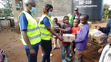 Two people handing a food package to a group of young children