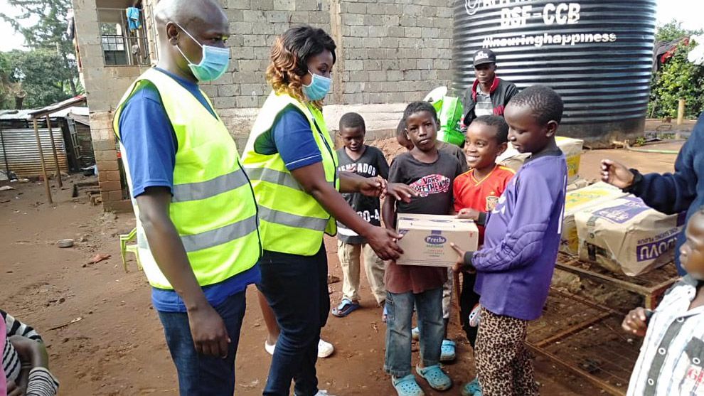 Two people handing a food package to a group of young children