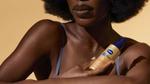 A Black woman holds Vaseline Radiant X Replenishing Hydrating Body Oil. Her arms, chest and lower face are visible.