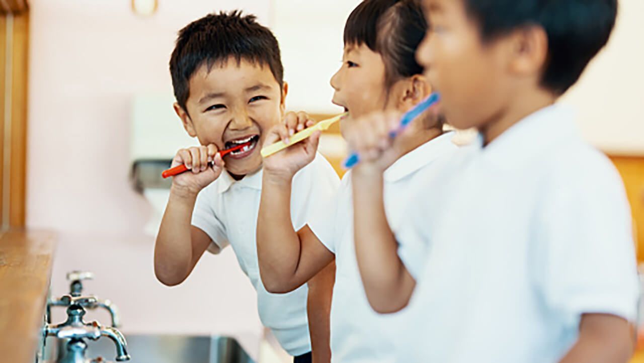 Troje osmjehnute djece koja peru zube