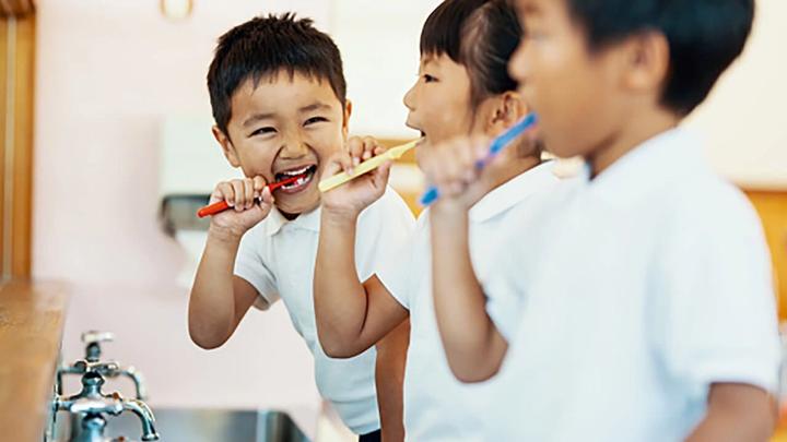 Tři usmívající se děti si čistí zuby