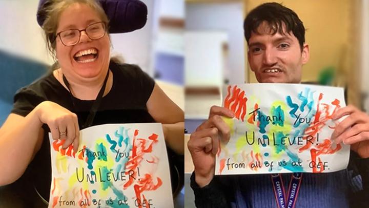 Two wheelchair users smiling and holding up paitings