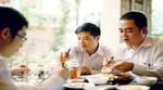 Three Vietnamese businessmen sit round a table to enjoy lunch together