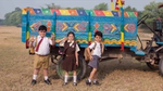 Three kids standing in front of a truck. Displaying the three swachh aadats of cleaning one’s hands, face and posterior.