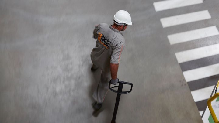 Worker in overalls and hard hat pulling a trolley across a factory floor