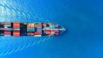An image of a boat from above, loaded with shipping containers, sailing on open water.
