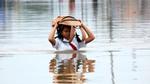 Schoolgirl wading through flood waters with her school bag above her head 
