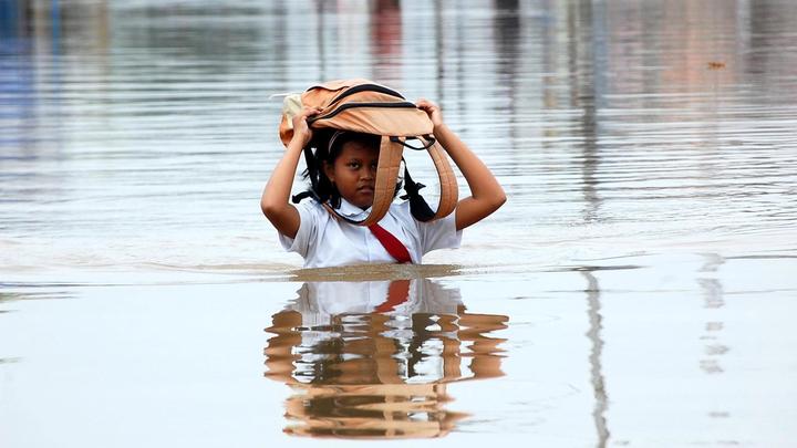 Schoolgirl wading through flood waters with her school bag above her head