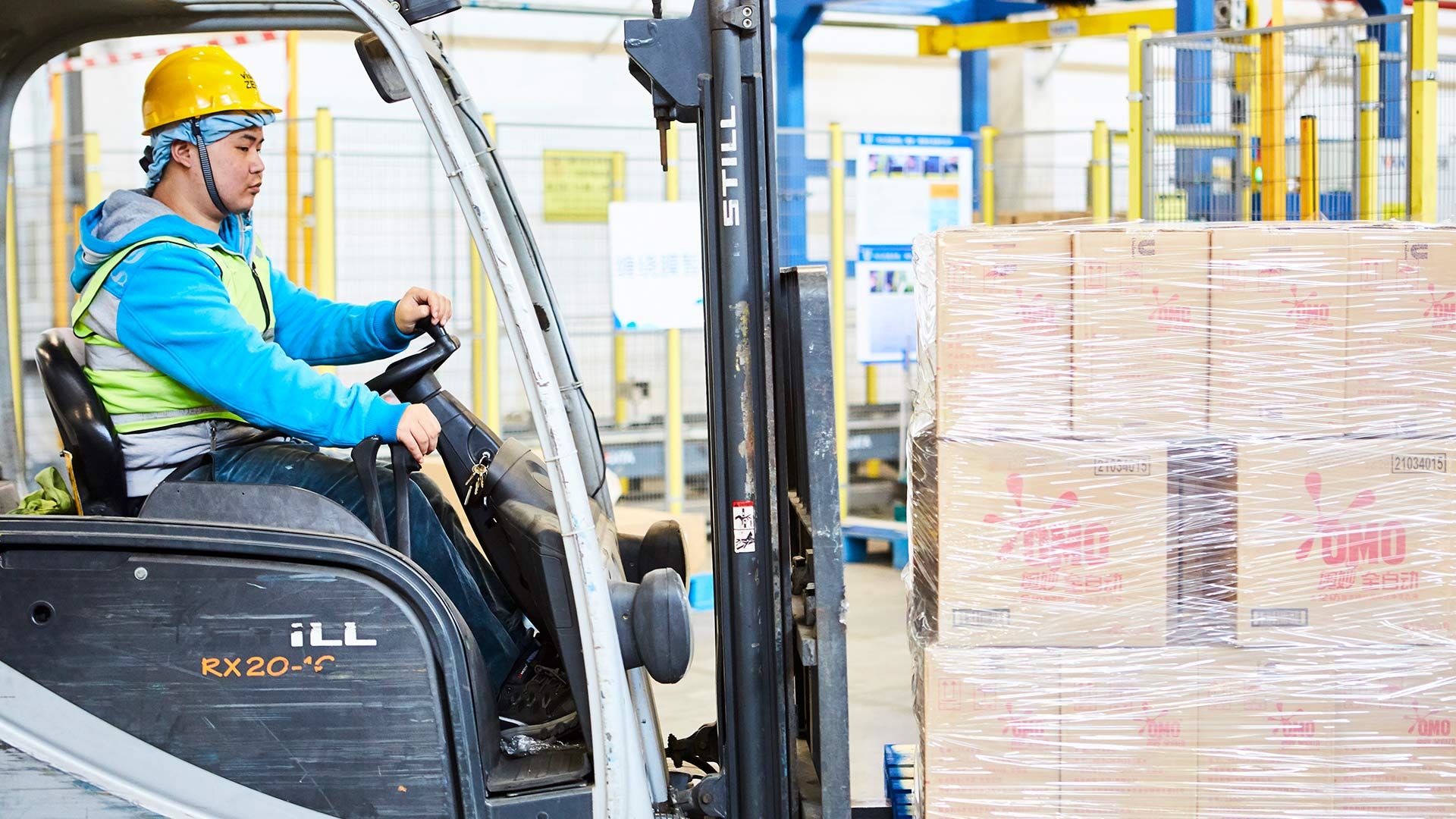 Fork lift truck driver moving a pallet of cardboard boxes labelled OMO in China