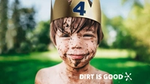 Young boy splashed in mud with a big grin, wearing a gold paper crown with a blue number four on the front.