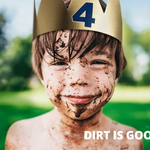 Young boy smiling, splashed in mud, wearing a gold paper crown.