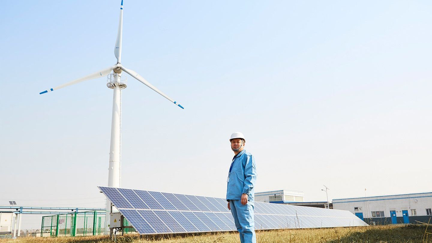 Worker in front of solar panels and wind turbine