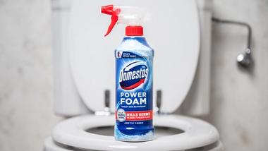 The new Domestos Power Foam Spray bottle sits on the edge of a bath. The bath and shower in the background are blurred