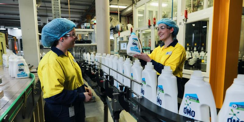 Factory workers standing over a line producing Omo liquid detergent