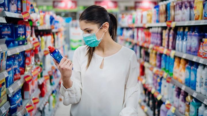 Une femme, portant un masque de protection, faisant des achats de produits de nettoyage dans un supermarché.