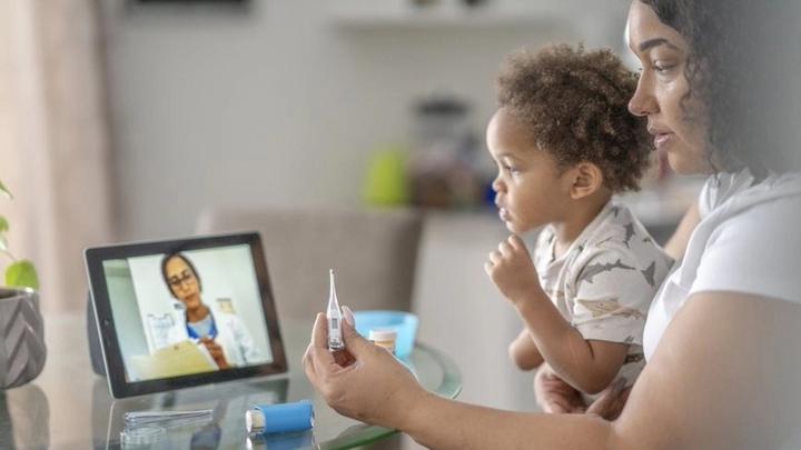 Woman with child on lap, discussing medicine with doctor via online appointment on her computer
